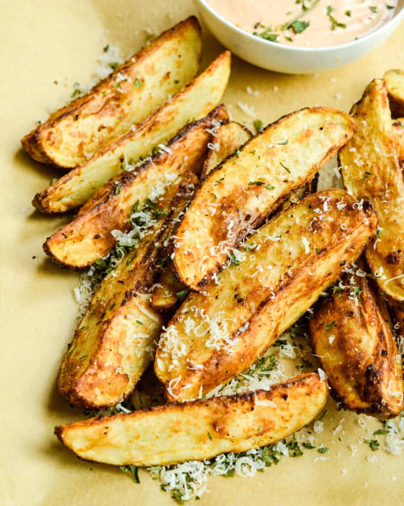 Fresh air fried potato wedges on a parchment paper coverd cutting board with chopped fresh thyme and Parmesan cheese. 