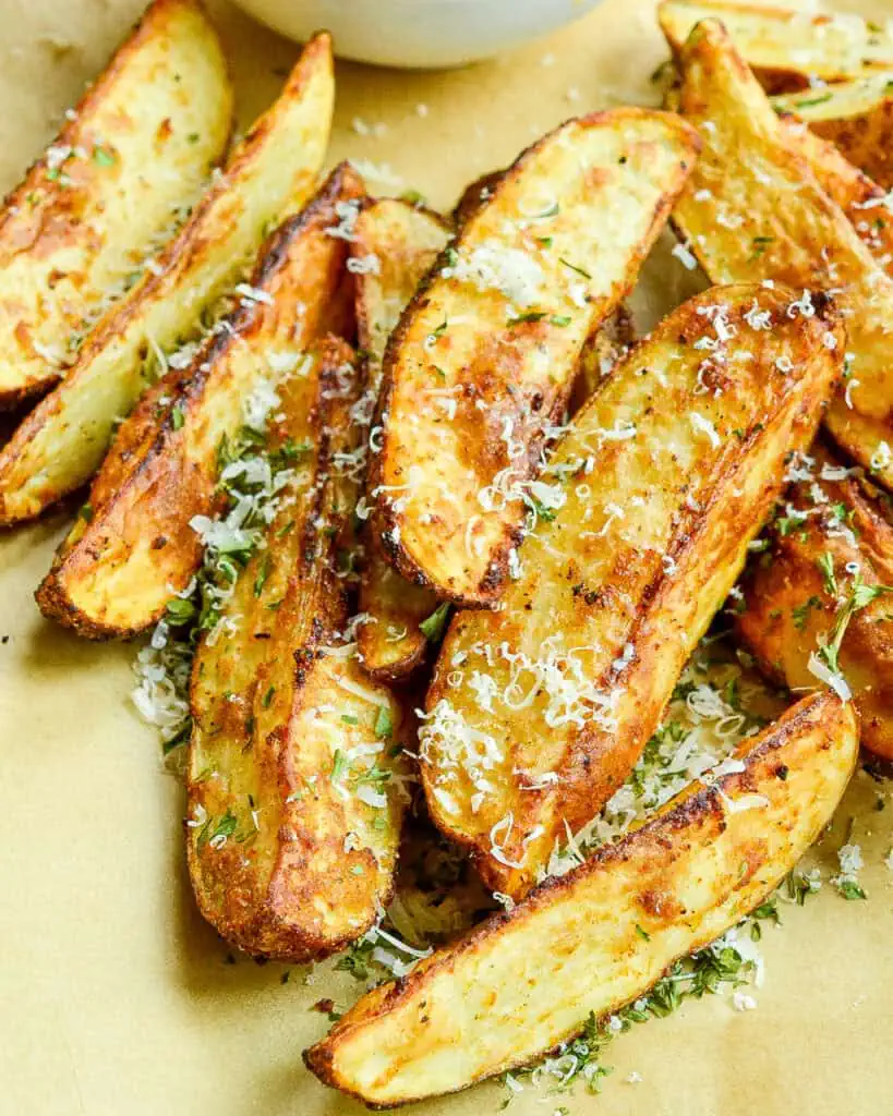 Air fryer potato wedges on parchement paper with Parmesan and chopped fresh thyme.