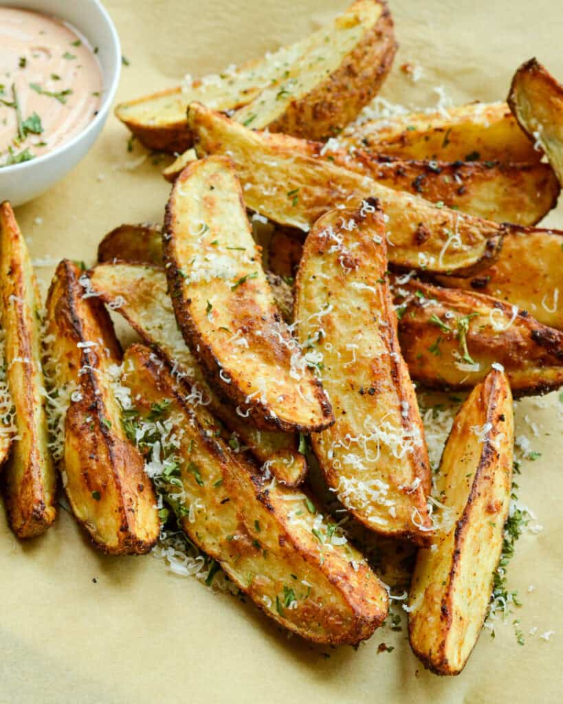 Air fried potato wedges on parchment paper with a bowl of comeback sauce. 
