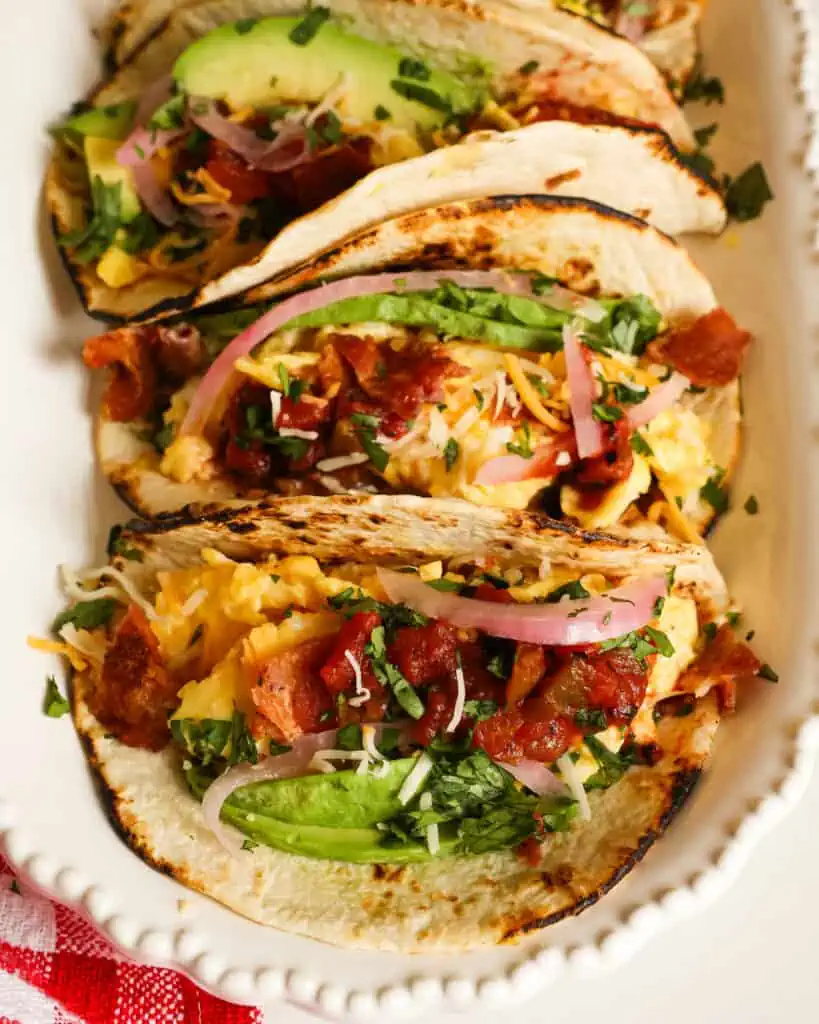These soft Breakfast Tacos are loaded with protein from bacon, scrambled eggs, cheddar cheese, and Monterey Jack Cheese, all wrapped in a tortilla and topped with salsa, avocado, pickled red onions, and chopped fresh cilantro. 