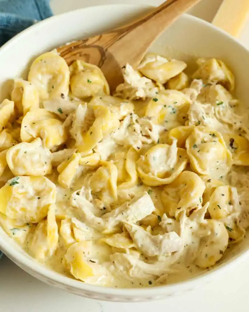 A serving bowl full of chicken tortellini alfredo with wooden spoon.