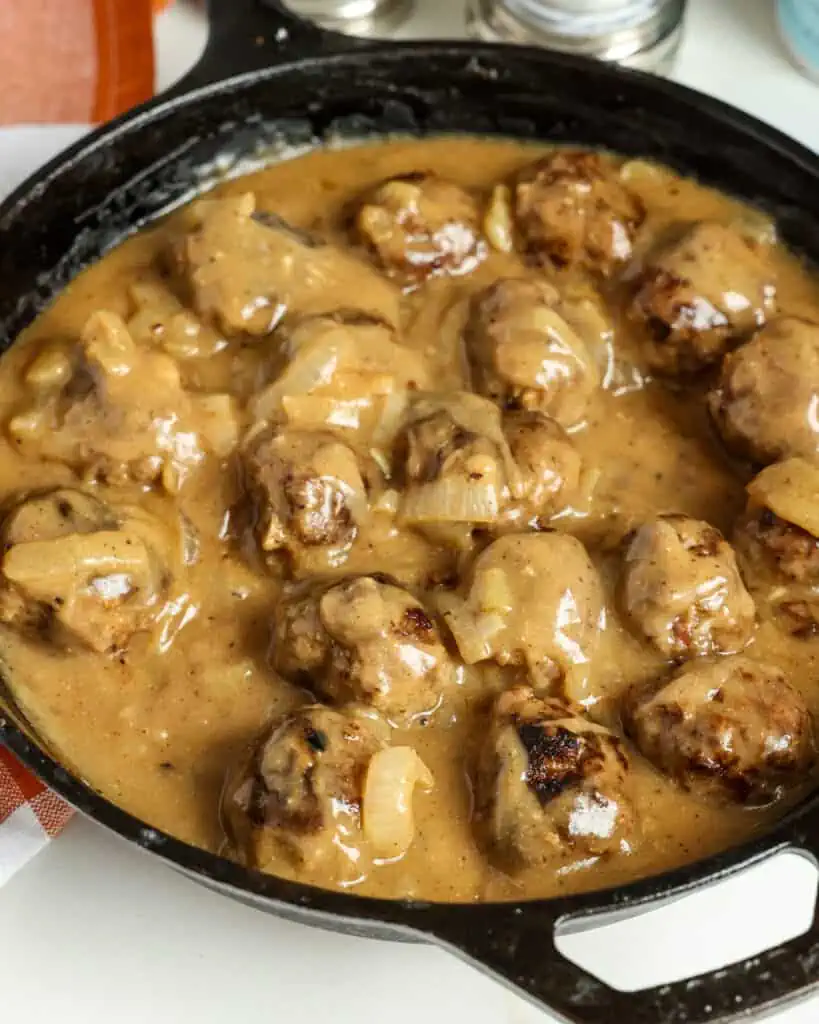 Schnell und einfach zubereitete Fleischbällchen werden mit Zwiebeln in der Pfanne gebraten und mit einer glatten, cremigen Soße aus Bratensaft übergossen und mit gemahlenem Pfeffer und gehacktem frischem Thymian gewürzt.