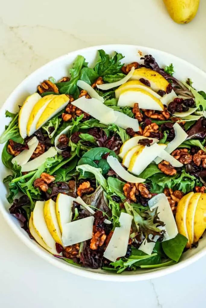 This Pear Salad combines candied walnuts, mixed greens, fresh pears, dried cranberries, and shaved Parmesan cheese, all drizzled with a homemade balsamic vinaigrette.