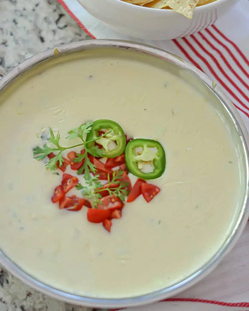 Small skillet full of queso cheese dip topped with jalapenos, red bell pepper, and cilantro. 