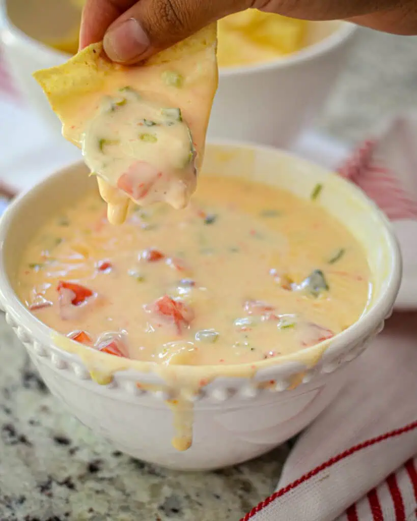 White Queso Dip A tortilla chip dipped in a bowl of queso cheese dip.