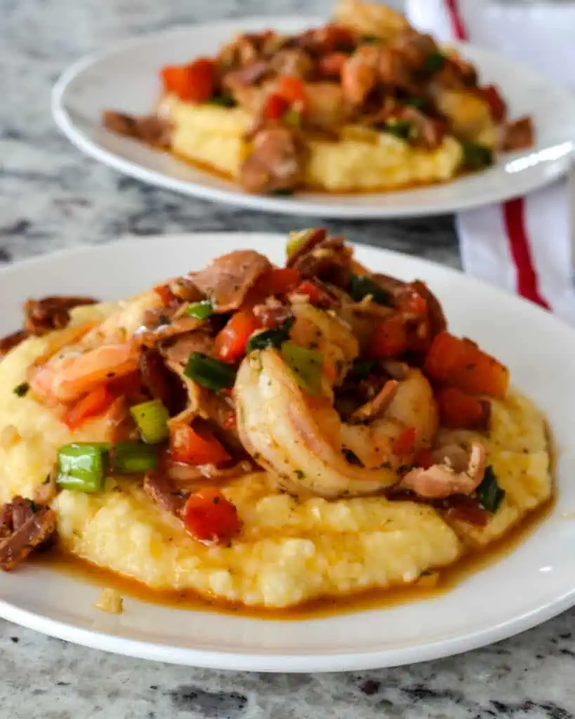 These delectable Shrimp and Grits are cooked with creole seasoning, red pepper, green onions, crisp bacon, and garlic over a bed of creamy cheddar grits.