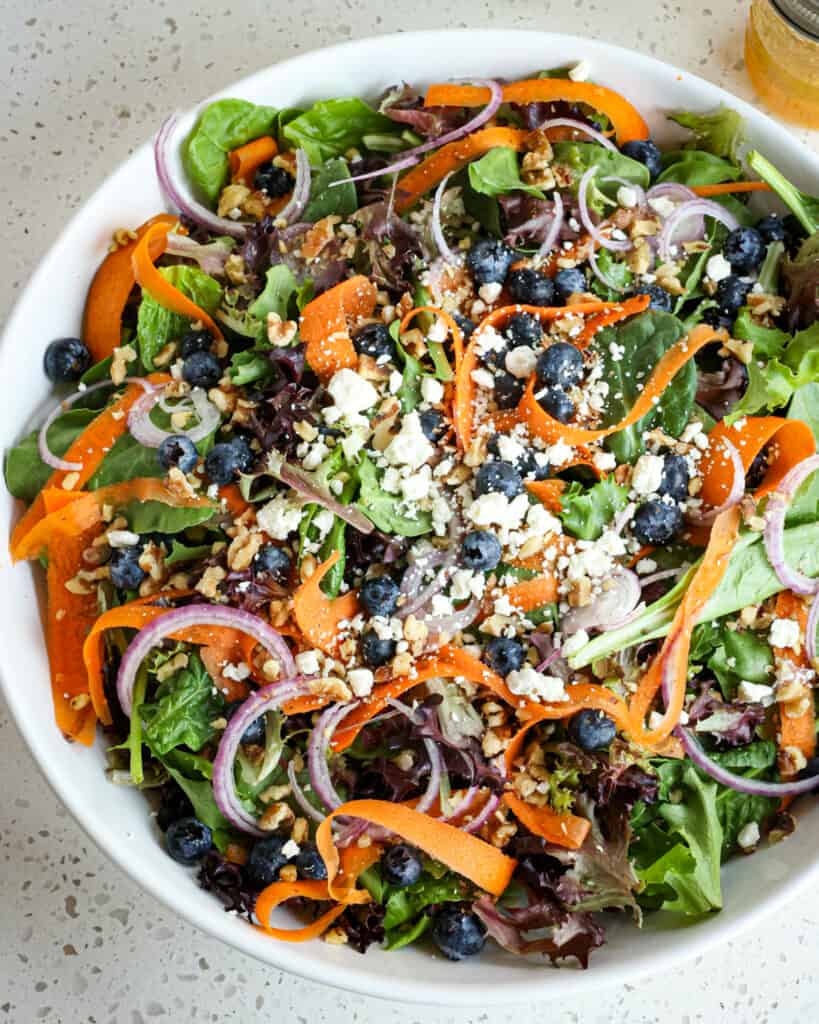 A big bowl of spring mix salad drizzled with an orange vinaigrette.  