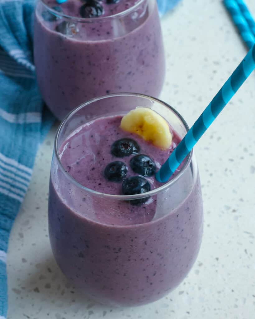Two blueberry smoothies garnished with blueberries an banana. 