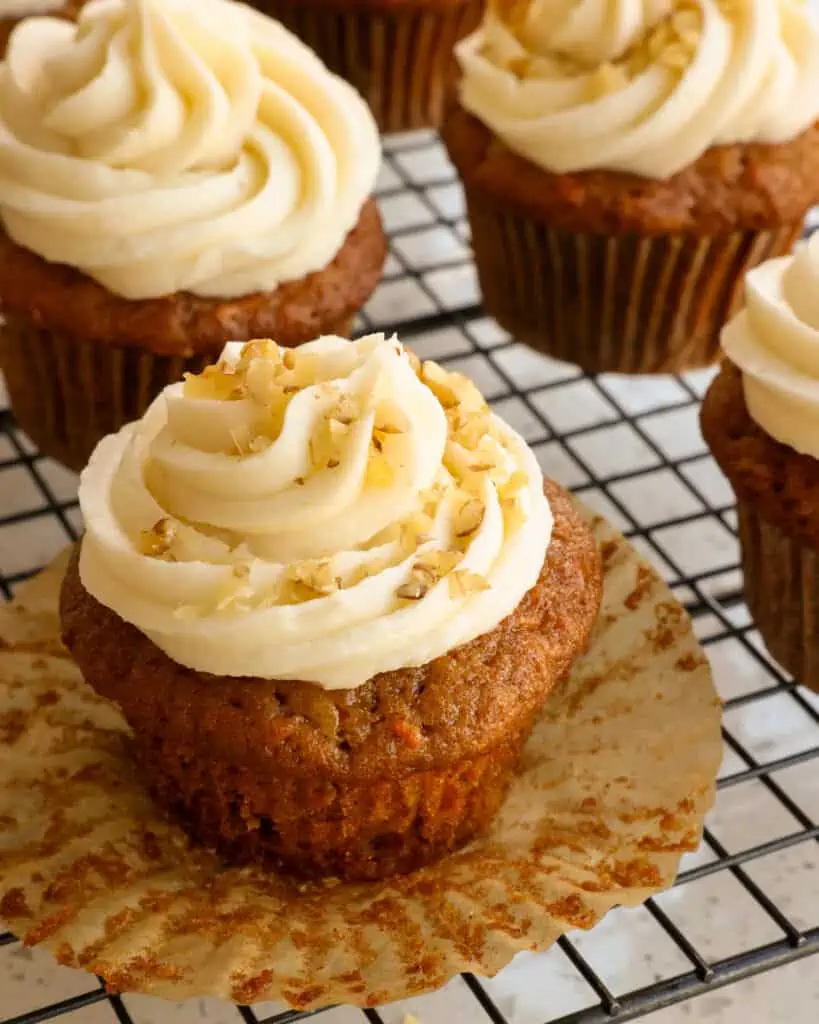 A cream frosted carrot cupcake sprinkled with nuts. 