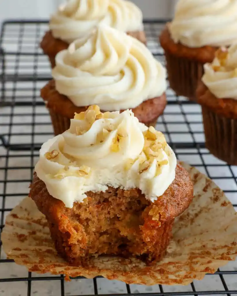 Carrot Cake Cupcakes with crushed pineapple and the perfect blend of spices, all topped with a homemade cream cheese frosting on a wire rack showing the inside of the cupcake. 
