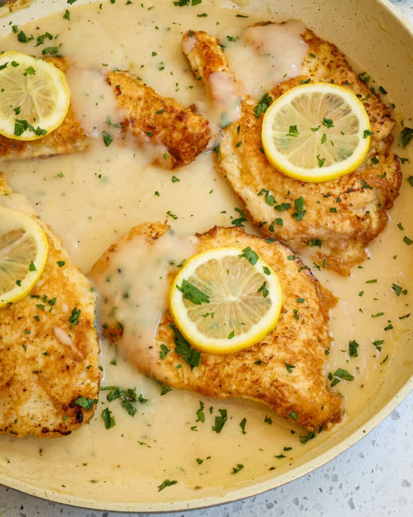 Chicken Francese topped with lemon slices and chopped fresh parsley in a large skillet.