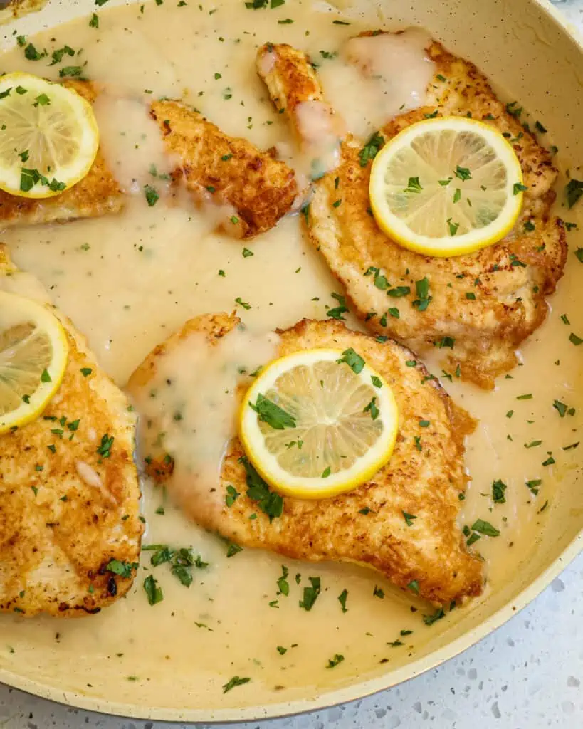 Chicken Francese topped with lemon slices and chopped fresh parsley in a large skillet. 
