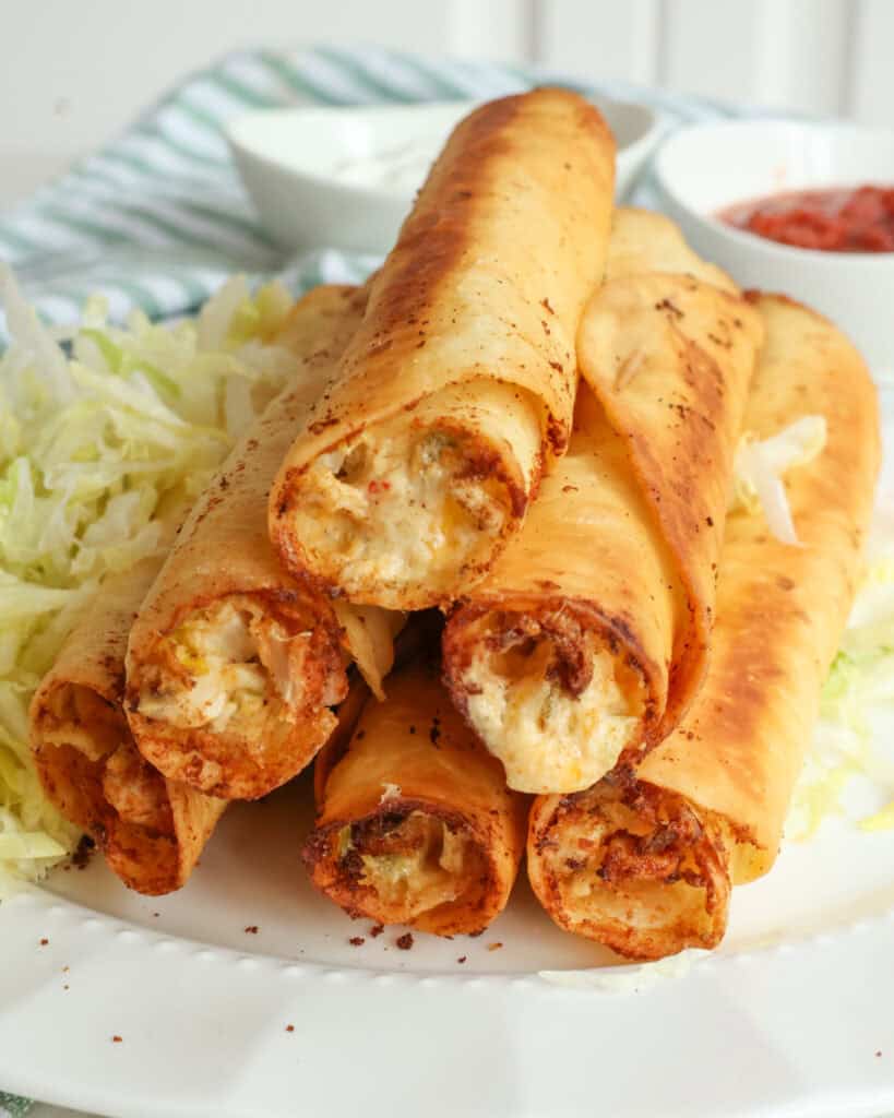 Fried chicken taquitos on a white plate with shredded lettuce. 