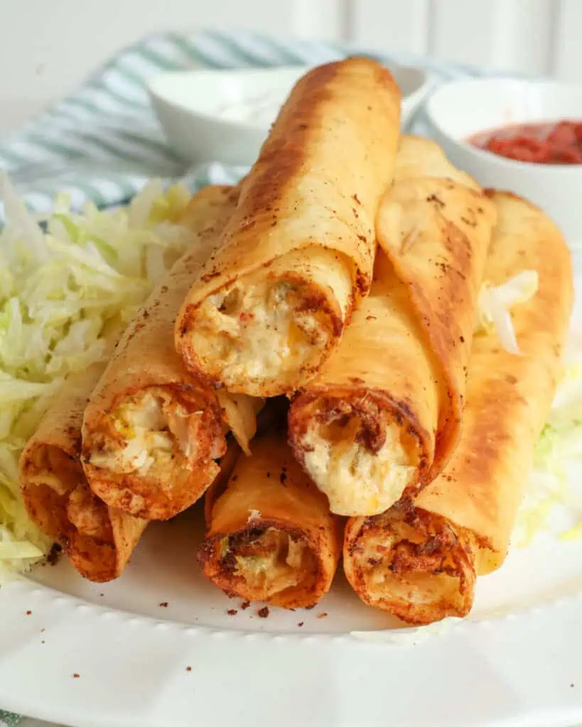 Fried chicken taquitos on a white plate with shredded lettuce. 