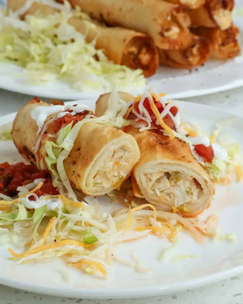 A chicken taquito cut in half on a plate with lettuce, sour cream, salsa, and cheddar cheese. 