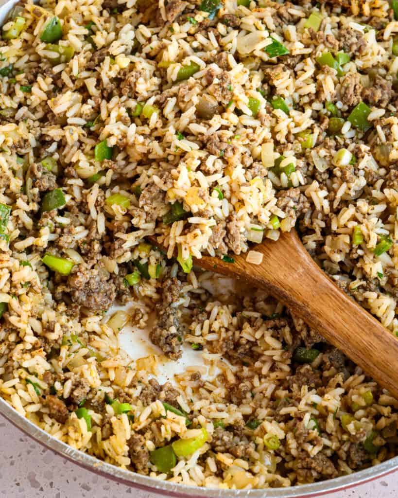 A large skillet full of dirty rice with a wooden spoon in it. 