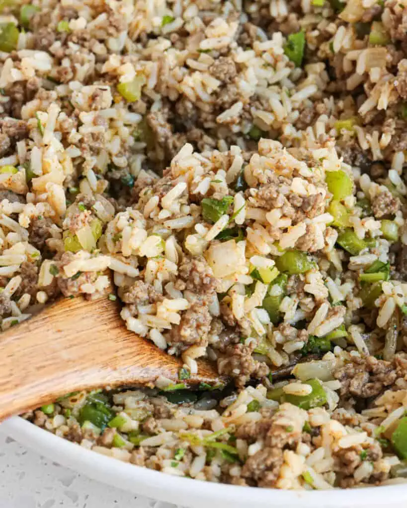 A serving bowl full of dirty rice with a wooden spoon in it. 