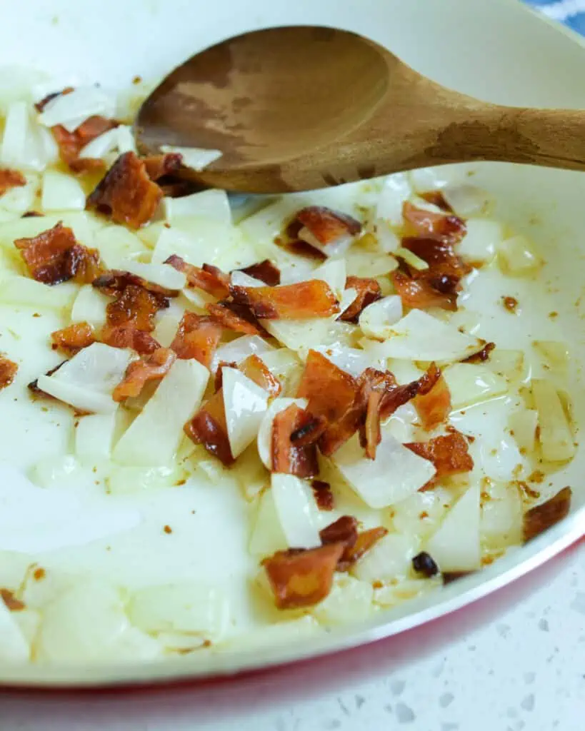 A skillet with bacon and fried onions. 