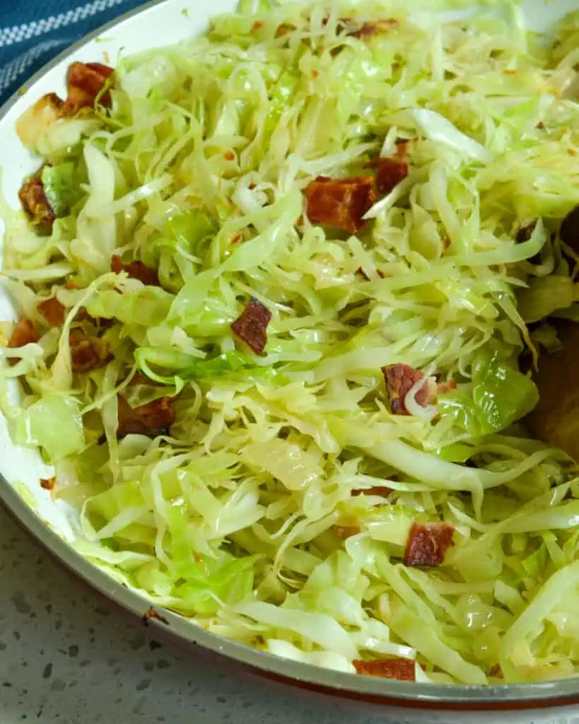 A large skillet full of fried cabbage, bacon, and onions with a wooden spoon in it. 