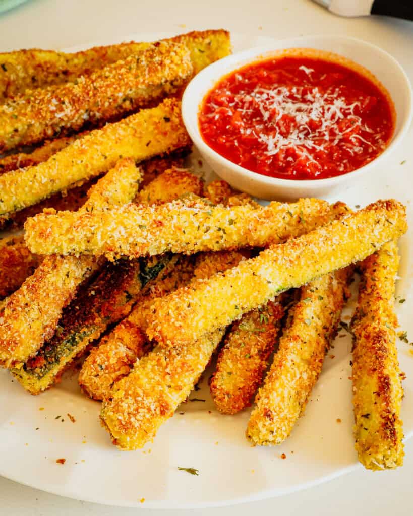 Stacks of fried zucchini on a serving plate sprinked with Parmesan cheese. 