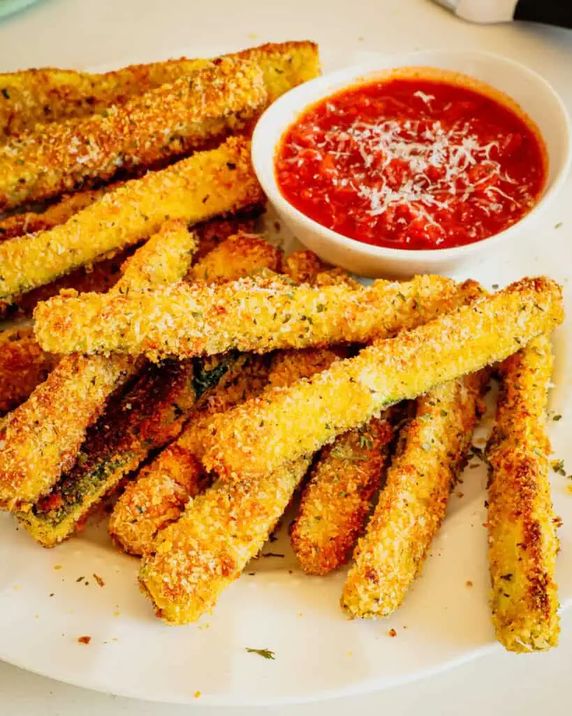 Stacks of fried zucchini on a serving plate sprinked with Parmesan cheese.