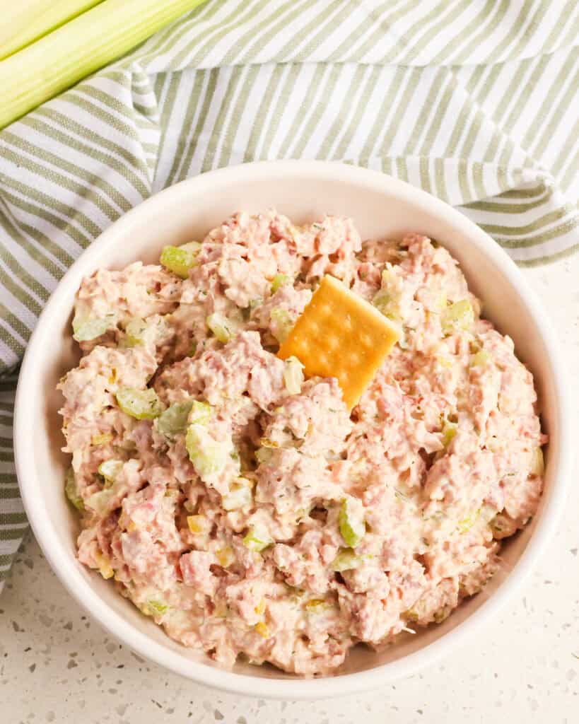 A bowl full of homemade ham salad with a cracker in it. 
