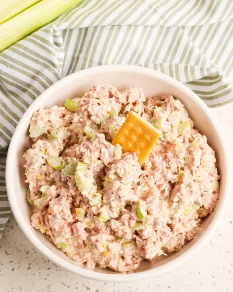 A bowl full of homemade ham salad with a cracker in it. 