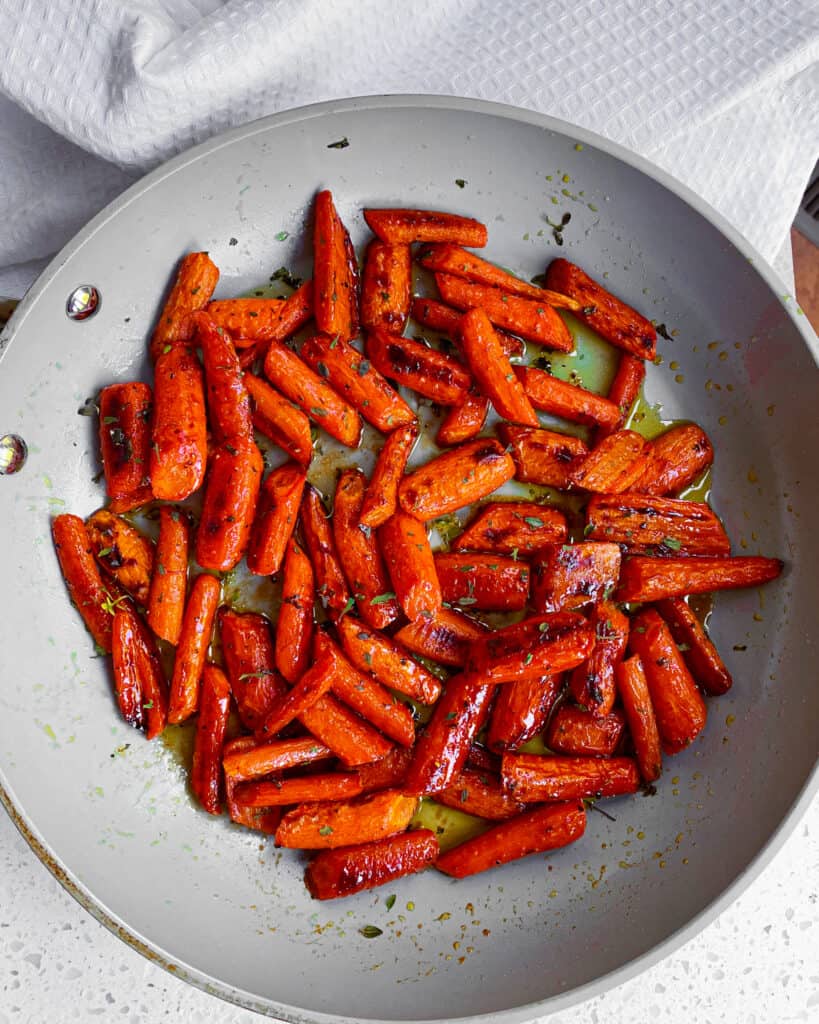Roasted carrots sprinked with fresh thyme in a large skillet. 