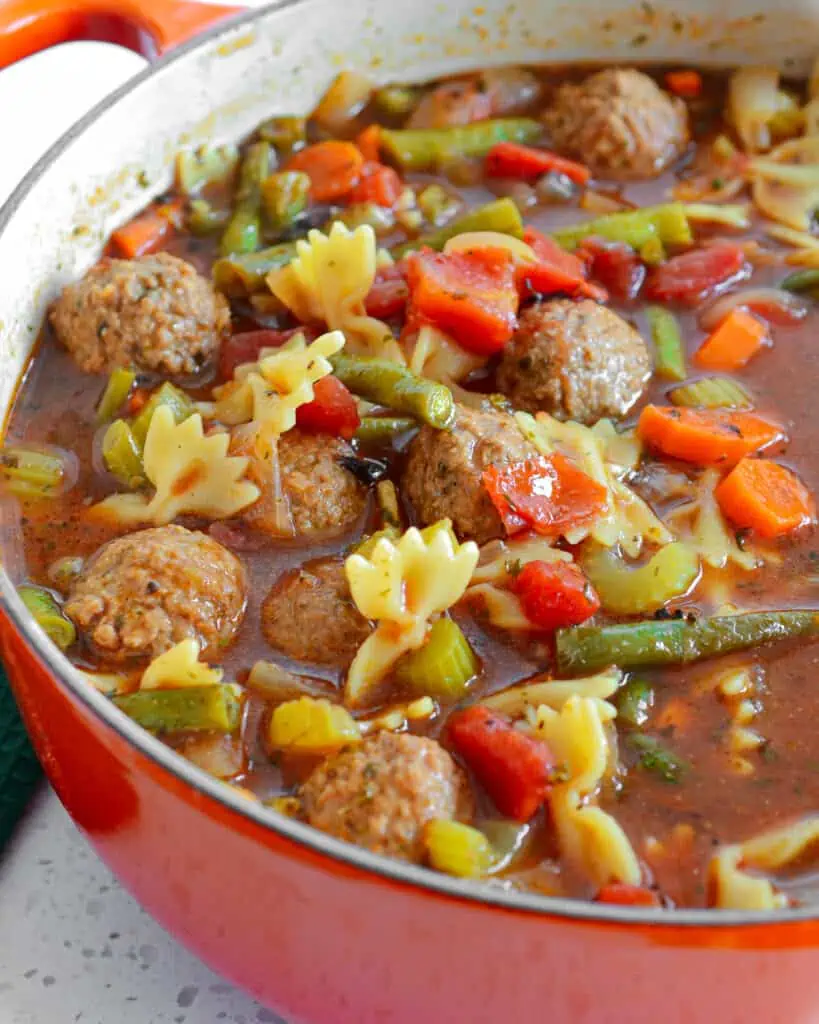A large pot of meatball soup made with meatballs, carrots, celery, tomato and green beans. 