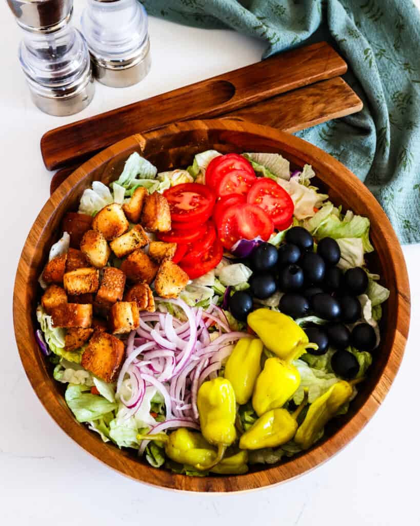 A wooden bowl full of olive garden salad. 