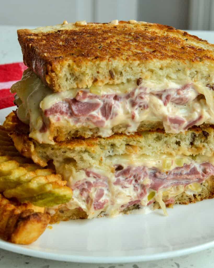 Reuben Sandwich is piled high with melty Swiss cheese, thin layers of sliced corned beef, sauerkraut, and homemade thousand island dressing, all on rye bread.