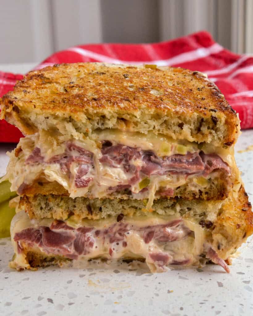 Reuben Sandwich is piled high with melty Swiss cheese, thin layers of sliced corned beef, sauerkraut, and homemade thousand island dressing, all on rye bread.