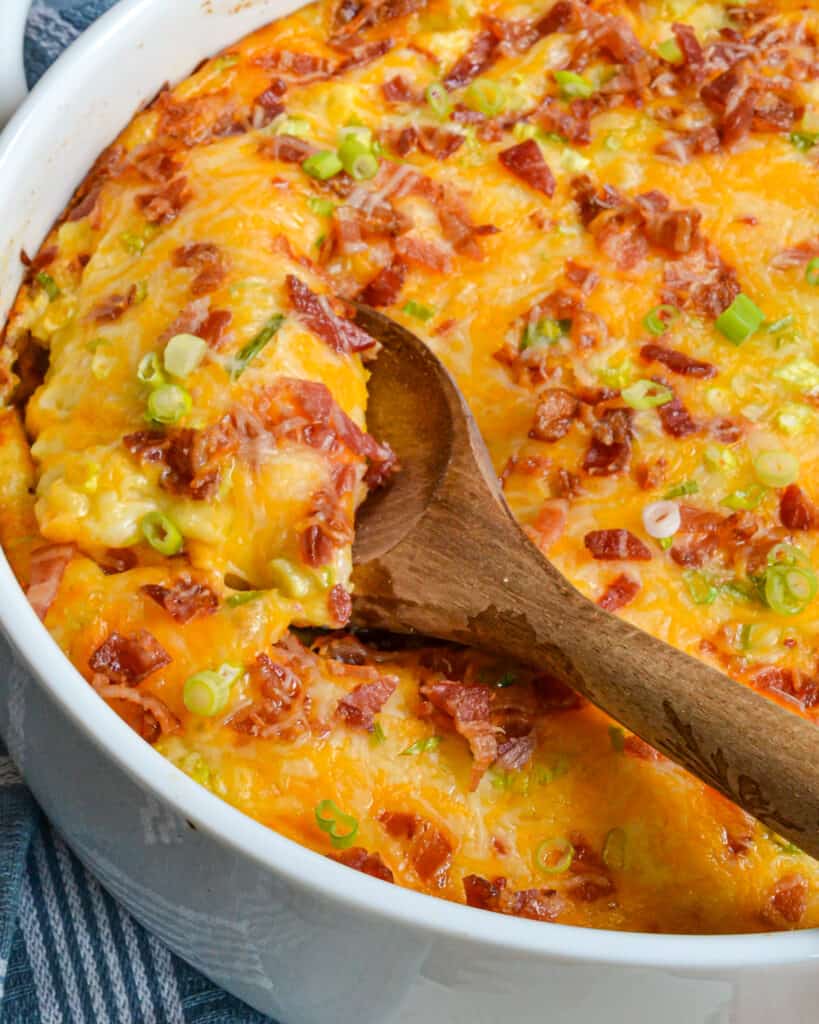 A large round casserole and wooden spoon full of twice baked potato casserole.