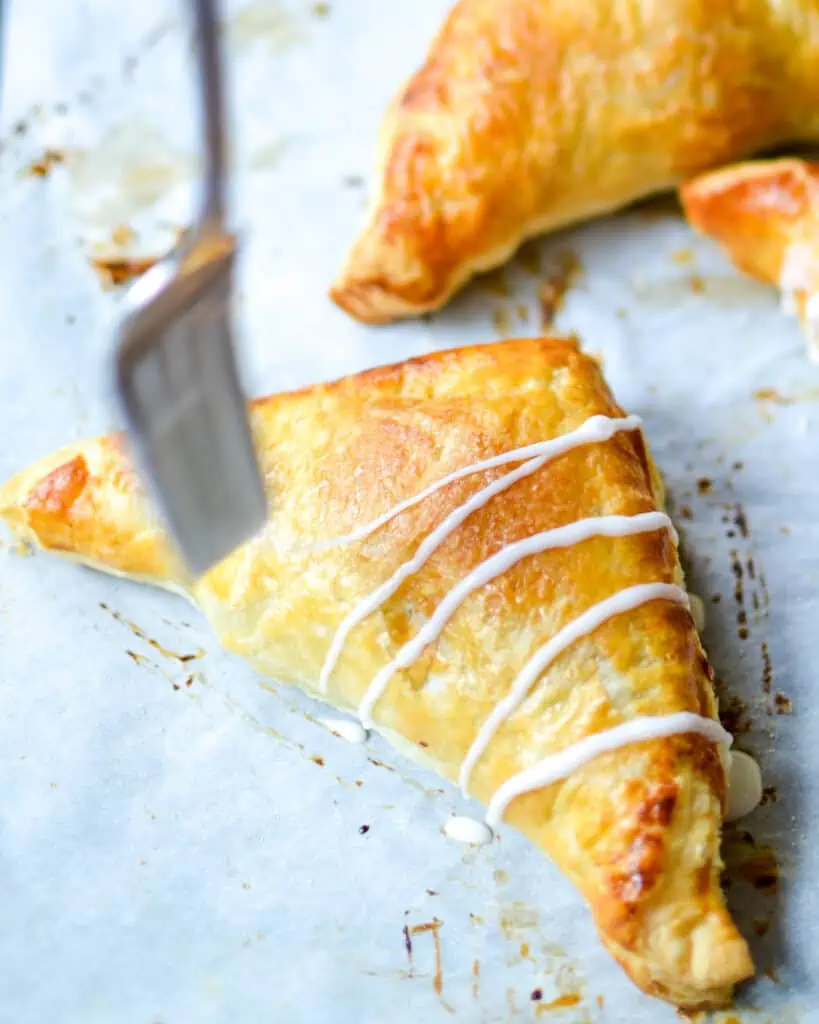 An apple turnover being drizzled with powdered sugar glaze. 