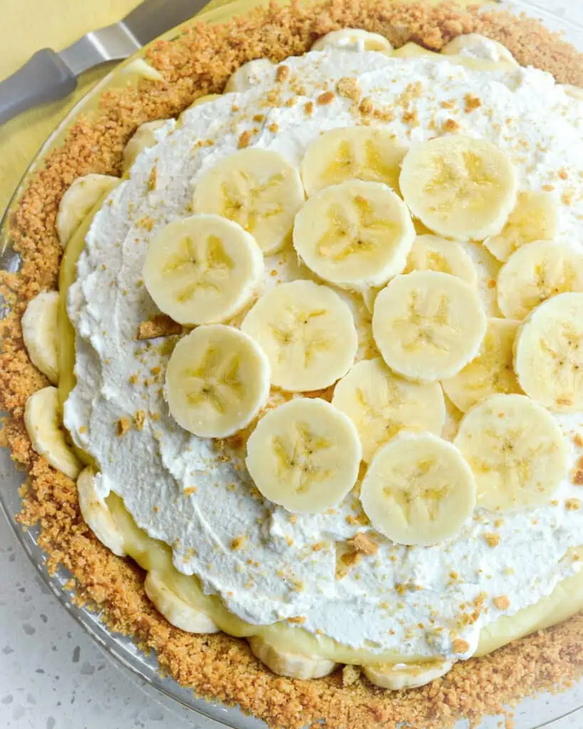 An overhead view of banana cream pie in a graham cracker crust topped with whipped cream and bananas. 