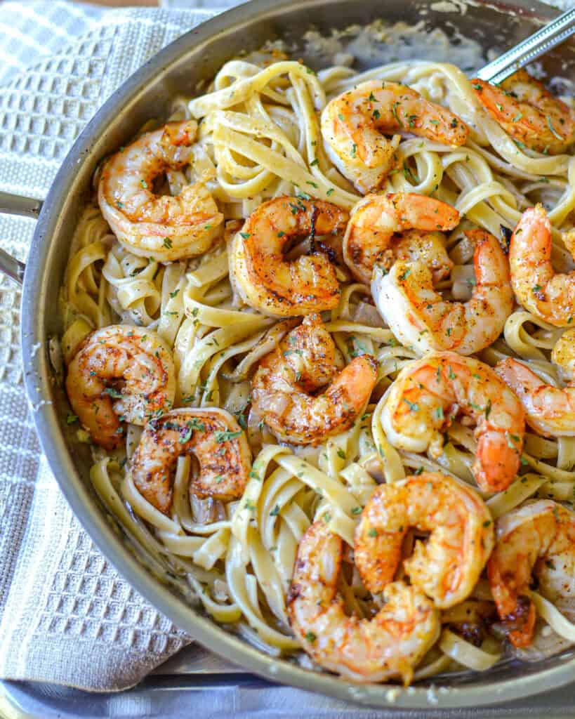 An overhead view of Cajun shrimp pasta in a large skillet with a spoon in it.
