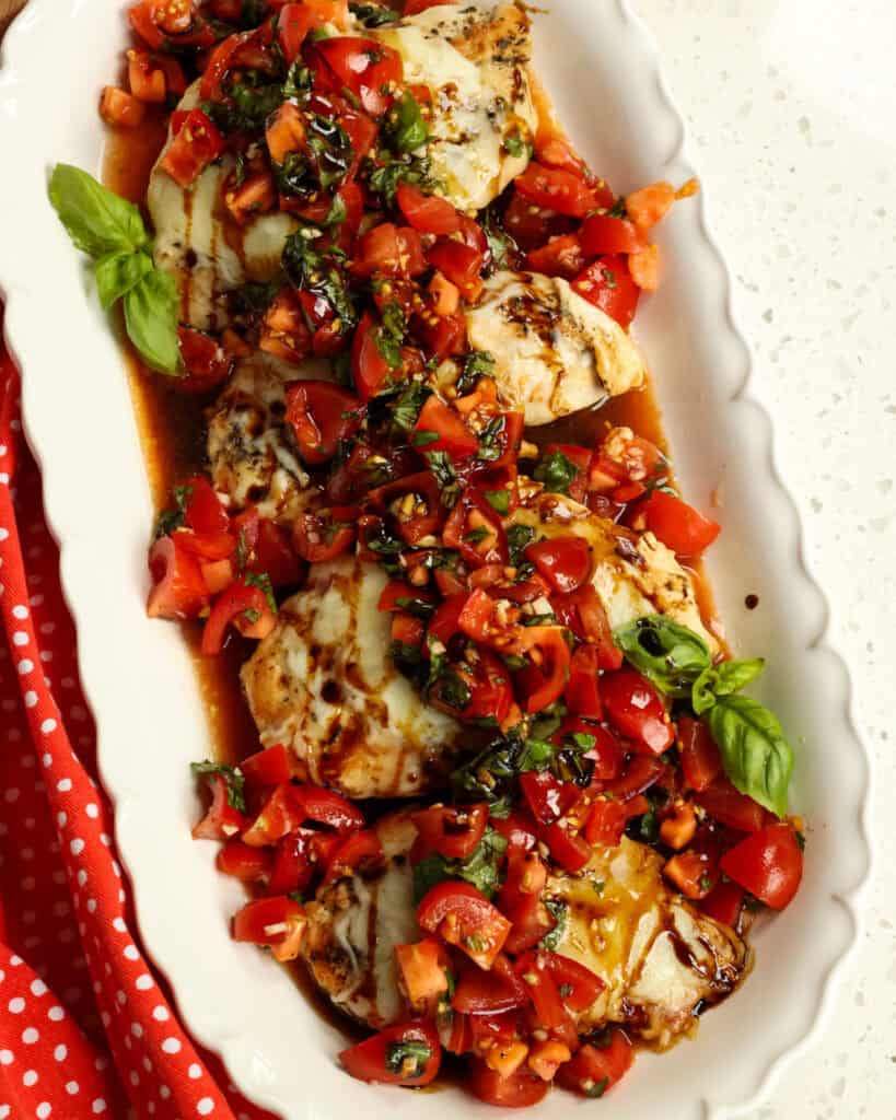 An overhead view of  Bruschetta Chicken on a white serving plater garnished with fresh basil. 