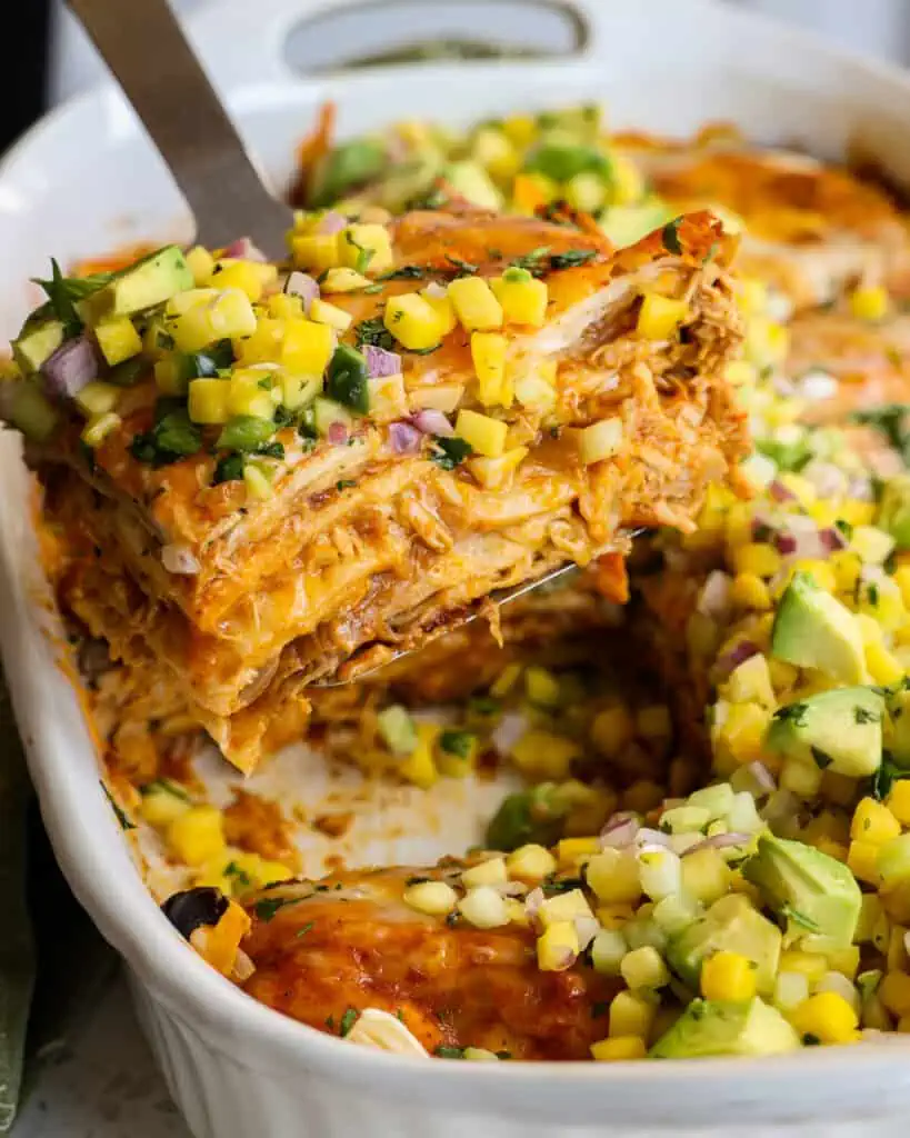 This flavor-packed Chicken Enchilada Casserole Recipe comes together quickly with layers of store-bought rotisserie chicken, tortillas, onions, garlic, and black beans, all smothered in enchilada sauce and topped with melted cheddar and Monterey Jack cheese.