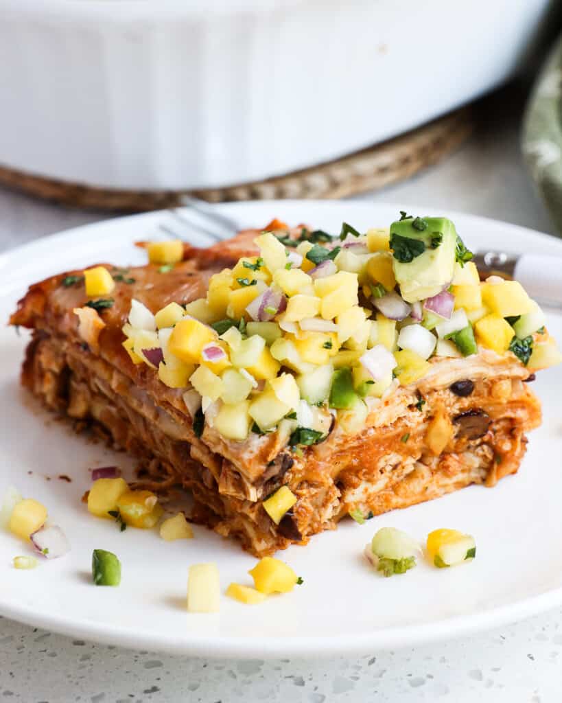 A slice of chicken enchilada casserole topped with pineapple salsa, avocado, and cilantro. 