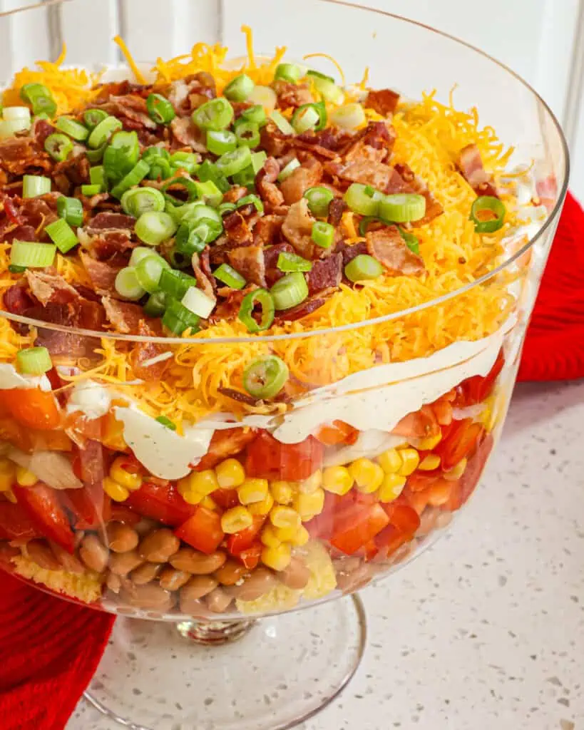 Layered Southern cornbread salad with bell pepper, tomatoes, bacon, cheddar, and ranch dressing in a trifle dish.  