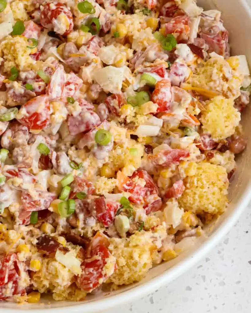 Southern Cornbread Salad Recipe is a delicious combination of flavors from moist cornbread, bell peppers, pinto beans, corn, tomatoes, ranch dressing, sharp cheddar cheese, bacon crumbles, and green onions.