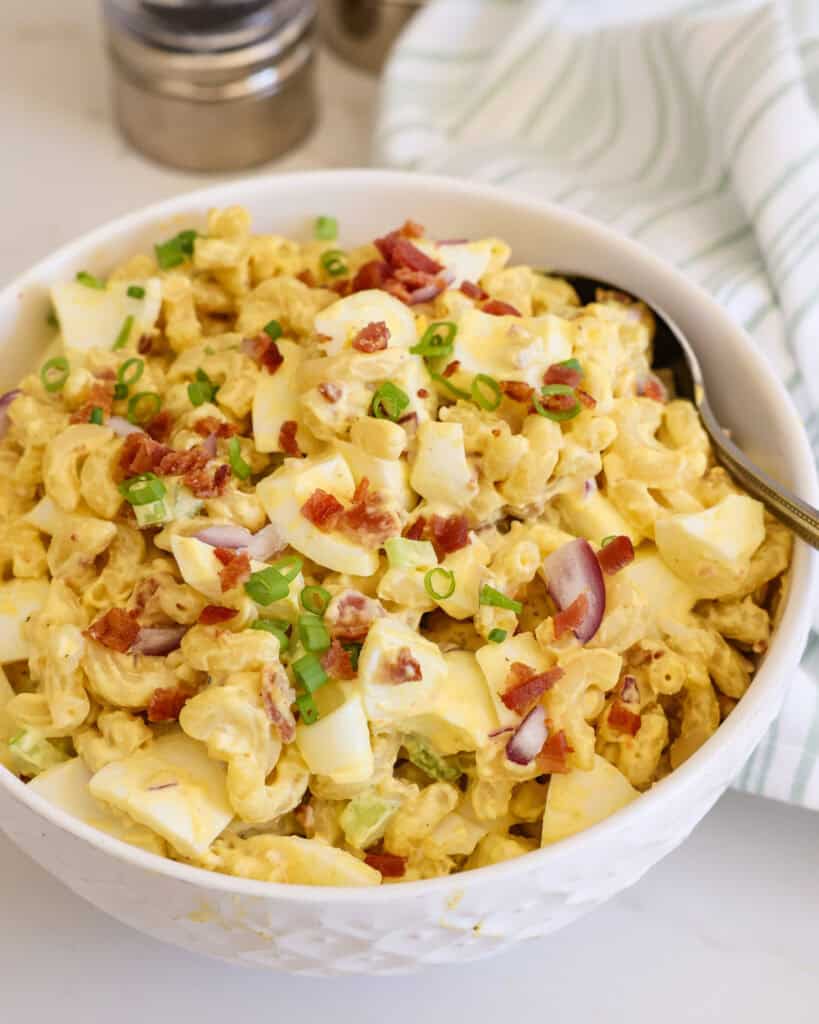 Deviled egg pasta salad in a white bowl with a metal spoon in it. 