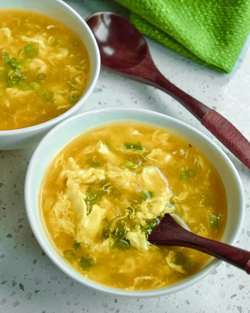 A bowl full of egg drop soup with a wooden spoon on the side. 