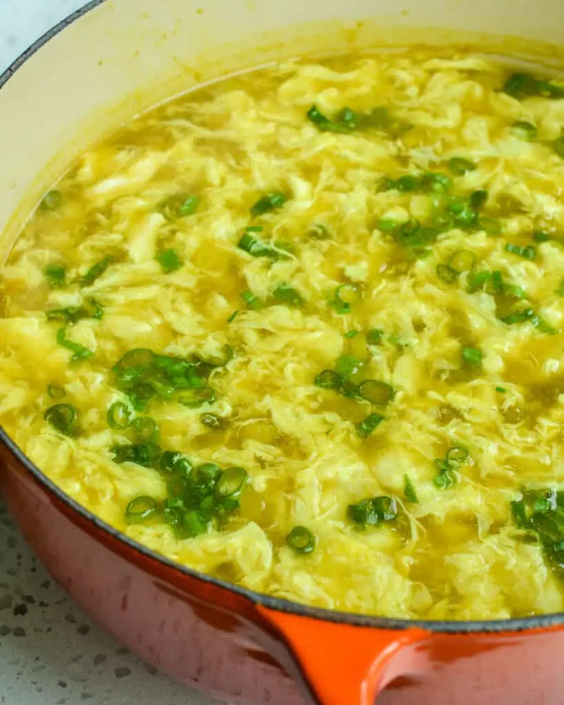 A close up view of a Dutch oven full of egg drop soup sprinkled with thin sliced green onions. 