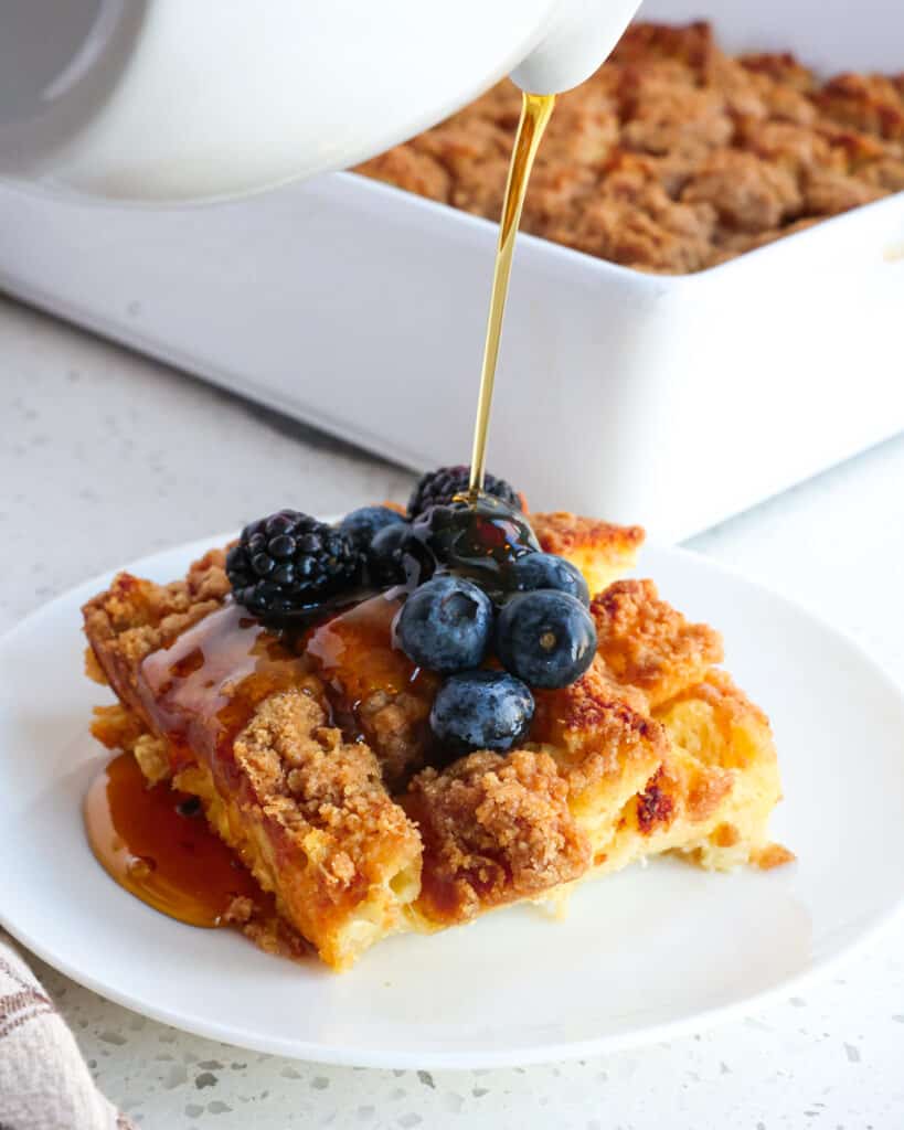 A single serving plate with French toast casserole topped with berries and maple syrup. 