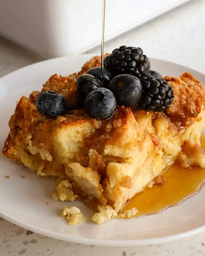 A slice of French toast casserole with blueberries and blackberries being drizzled with maple syrup.  