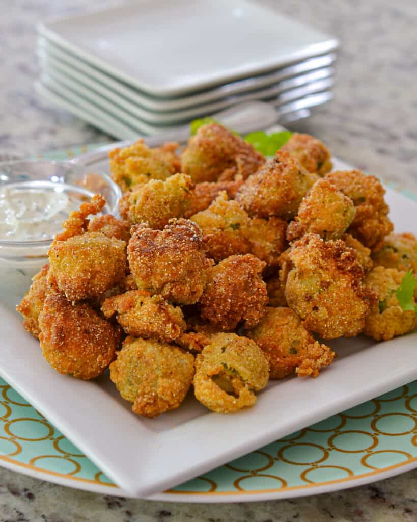 A close up view of fried okra on a plate with dipping sauce and appetizer plates in the background. 
