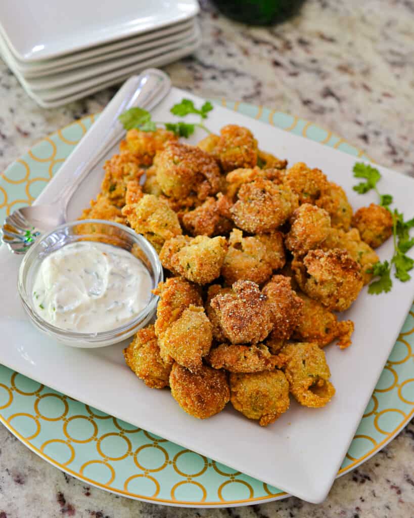 An overhead view of fried okra on a seerving plate with jalapeno yogurt dipping sauce. 
