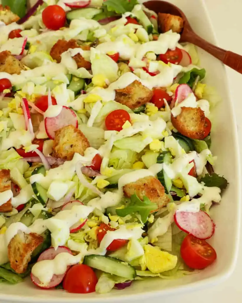 This easy garden salad combines iceberg lettuce with fresh vegetables like tomatoes, cucumbers, red onions, and radishes, all drizzled with a homemade buttermilk dressing and topped with chopped hard-boiled eggs and homemade croutons. 