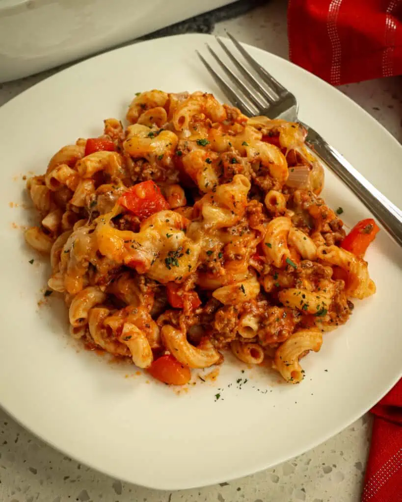 A single serving plate full of hamburger casserole with a fork and napkin on the side. 